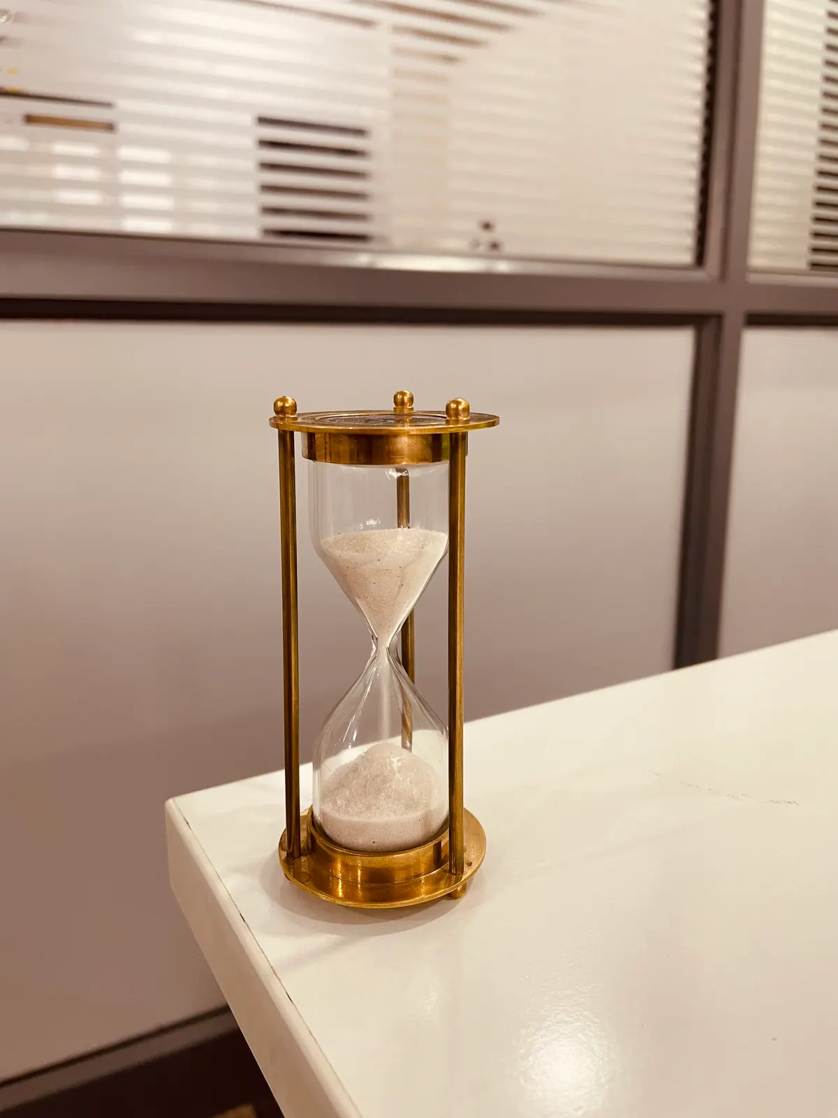 A small brass hourglass standing on the corner of a white desk