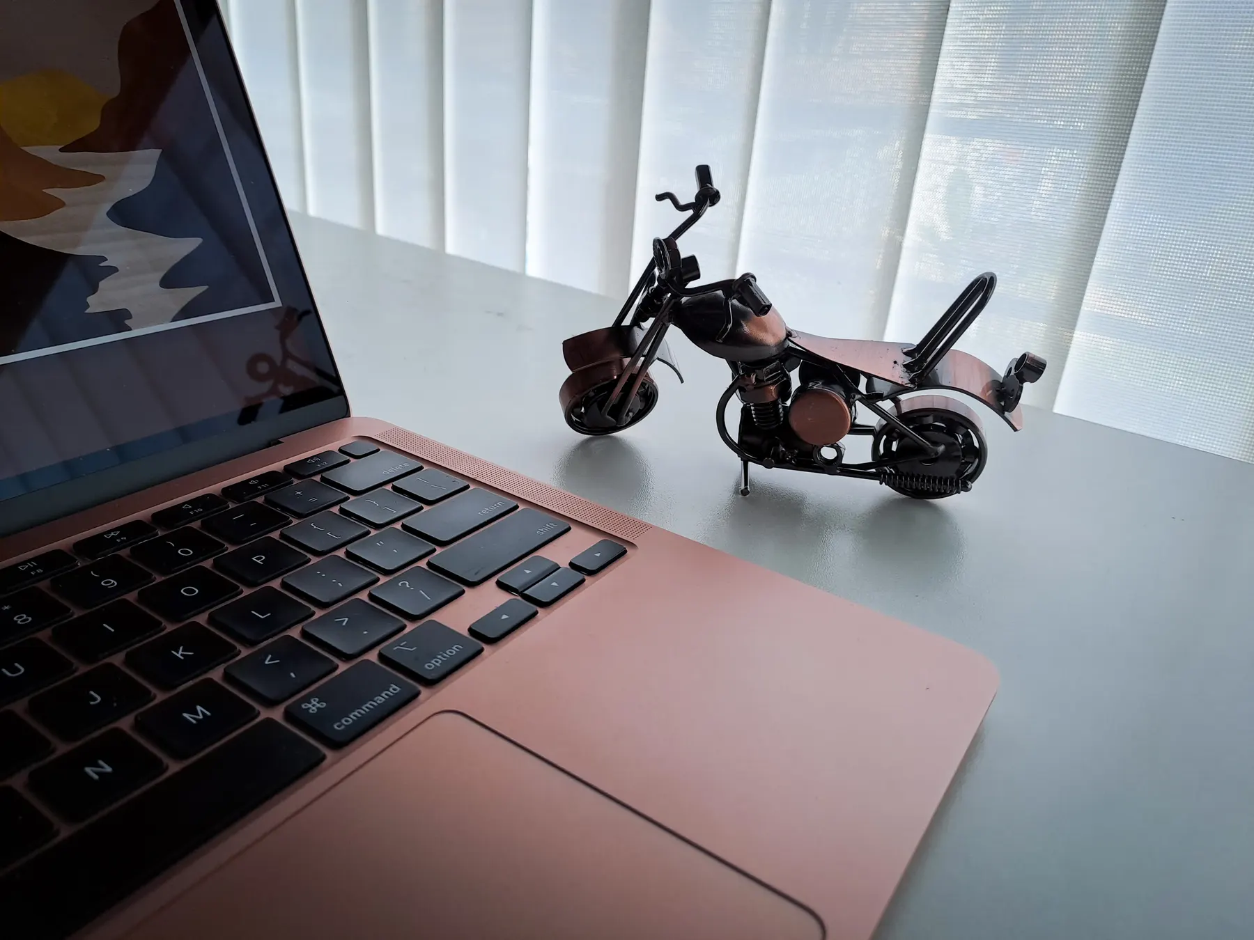 A laptop open on a bright desk beside a small metal motorcycle model