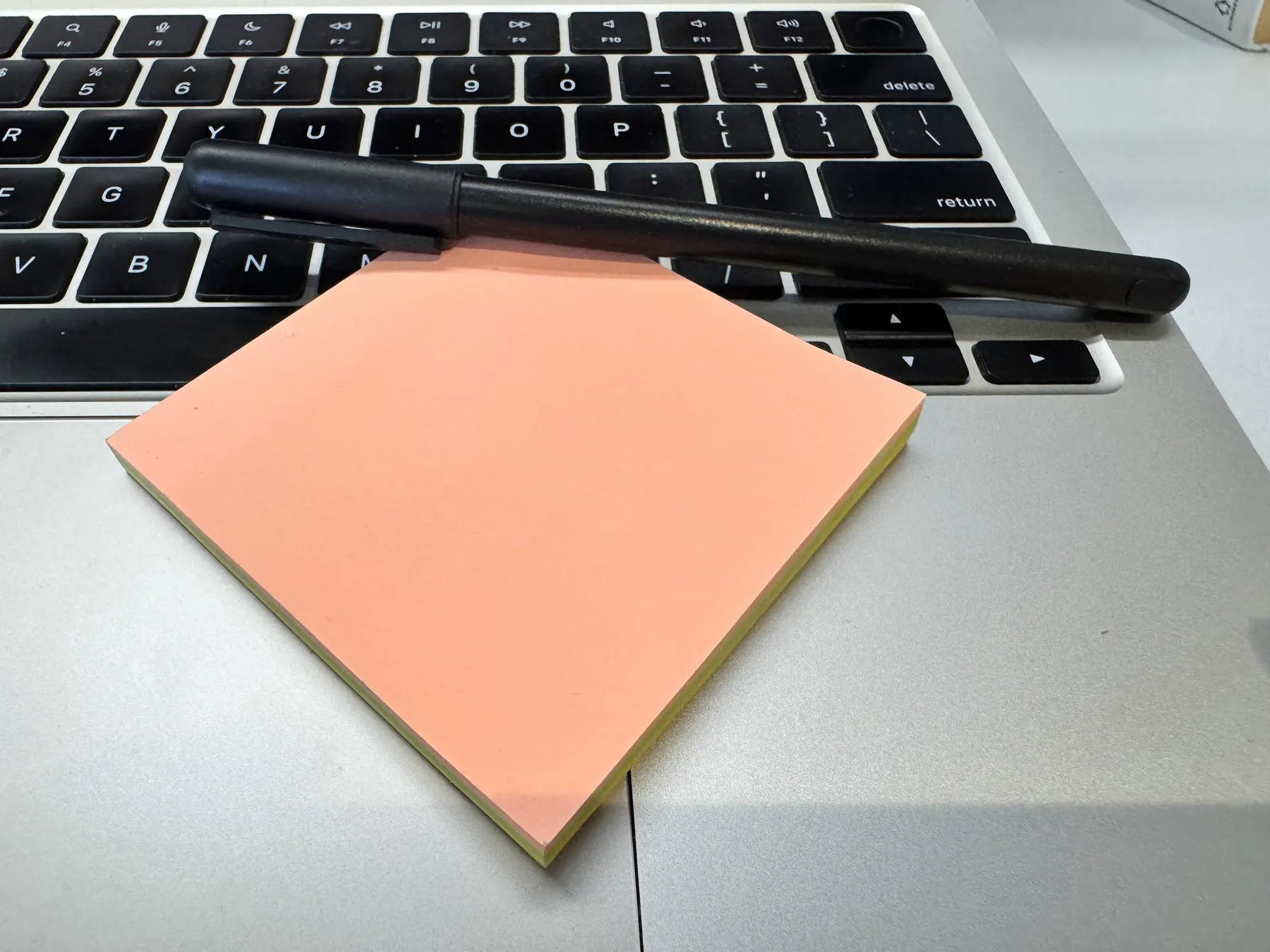 A pad of note paper and a pen resting on a laptop keyboard